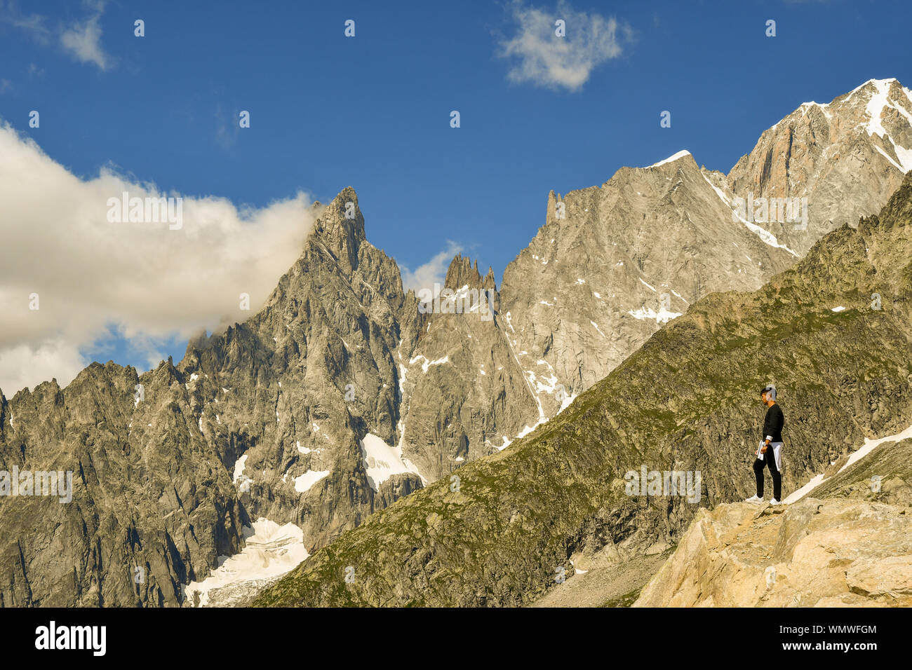 Jeune homme debout sur un rocher en admirant la vue sur le massif du Mont Blanc avec l'Aiguille Noire de Peuterey pic de montagne en été, Courmayeur, Italie Banque D'Images