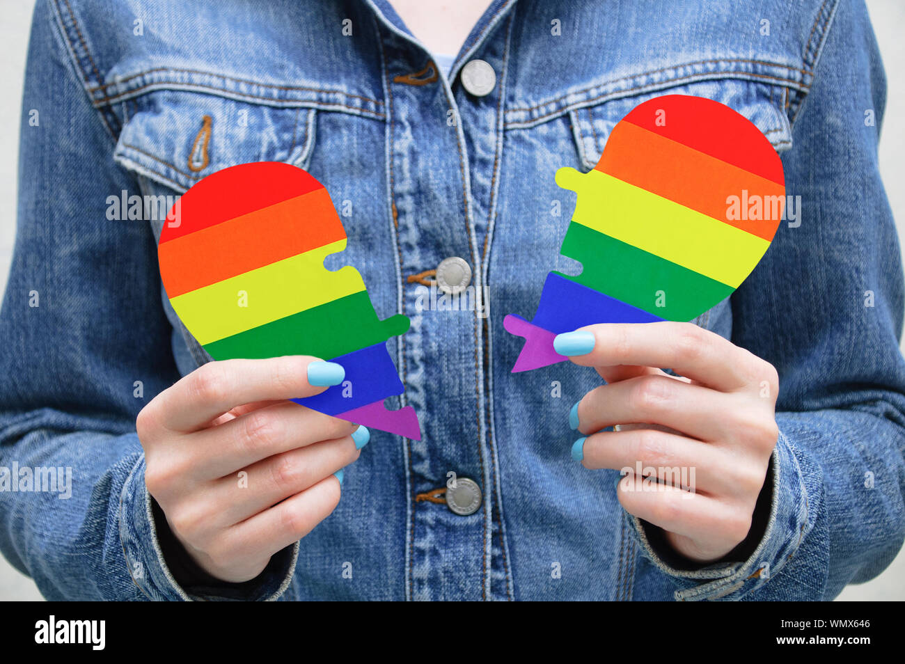 Moitiés du coeur avec symboles LGBT dans les mains d'une jeune fille de race blanche dans une veste en jean bleu. Banque D'Images