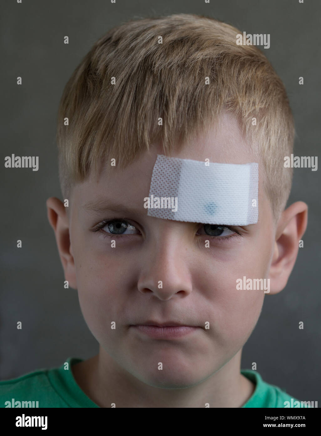 Close-up of Boy avec bandage sur front sur fond gris Banque D'Images