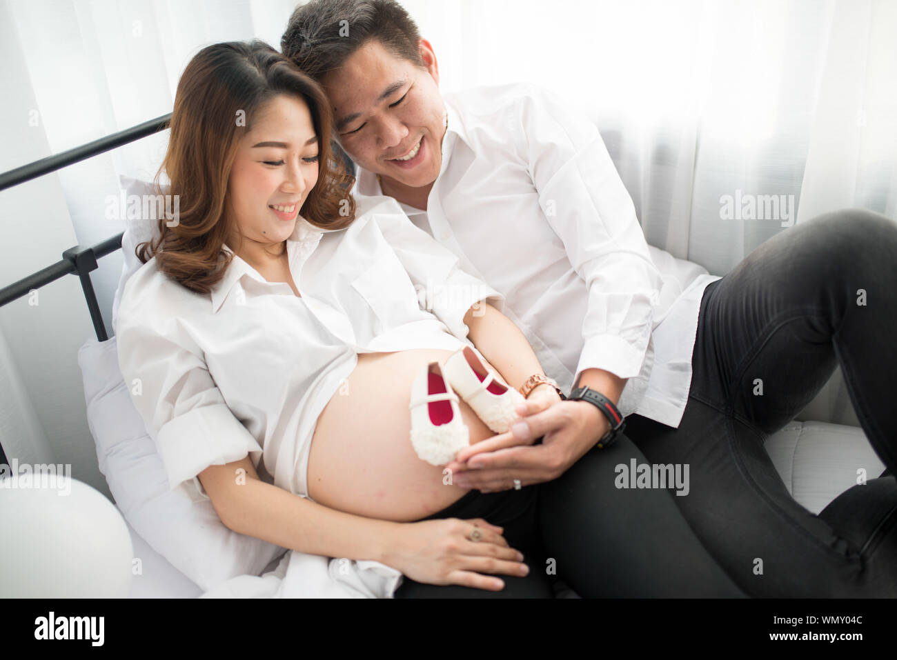 Femme enceinte avec l'homme à la recherche de chaussons pour bébé sur  l'Abdomen tout en vous relaxant sur le lit chez lui Photo Stock - Alamy