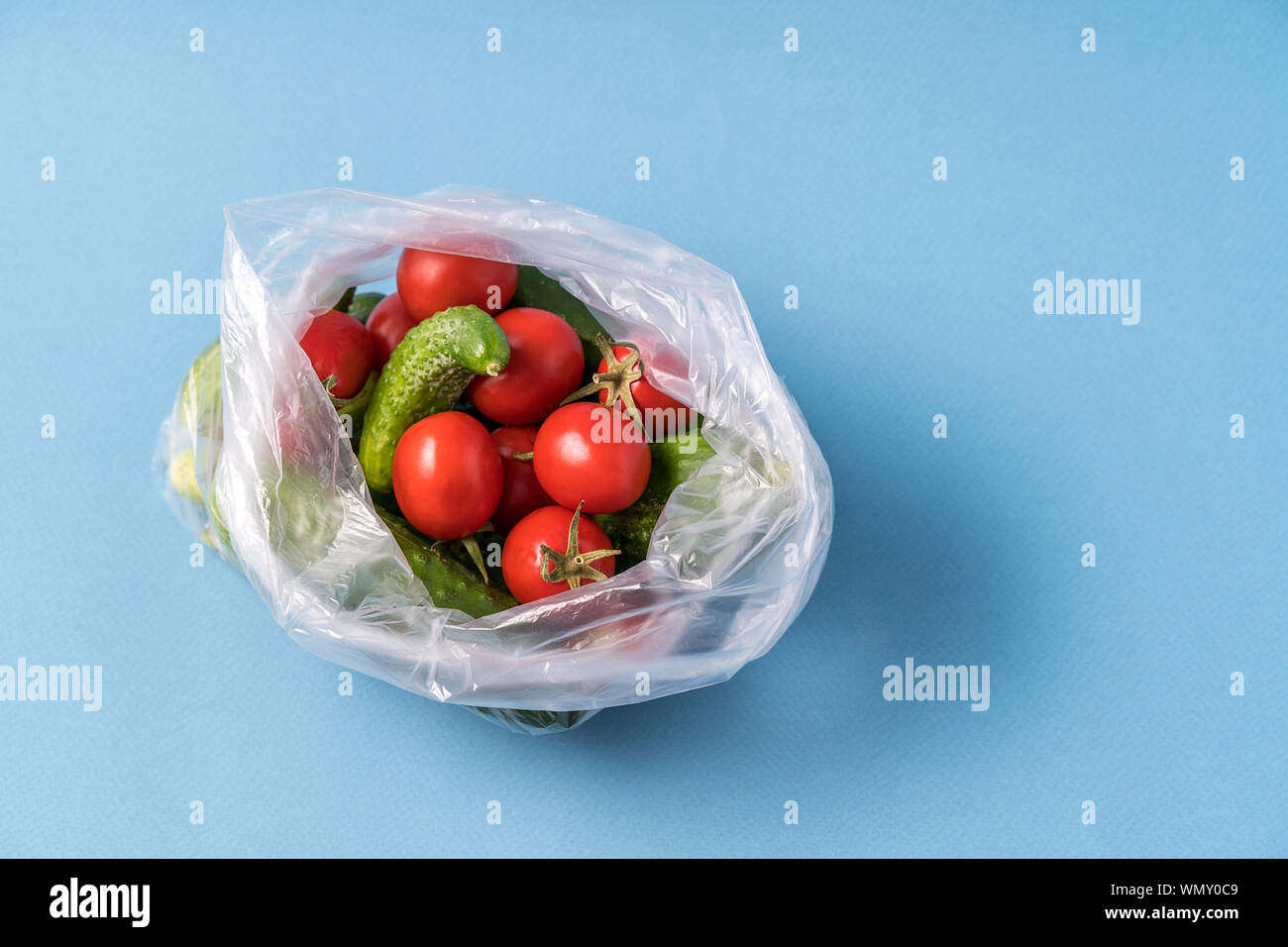 Vue de face des concombres et des tomates dans un sac plastique sur fond bleu. Image montre le harmness à l'aide de sacs de stockage de l'alimentation artificielle. Image horizontale. Banque D'Images
