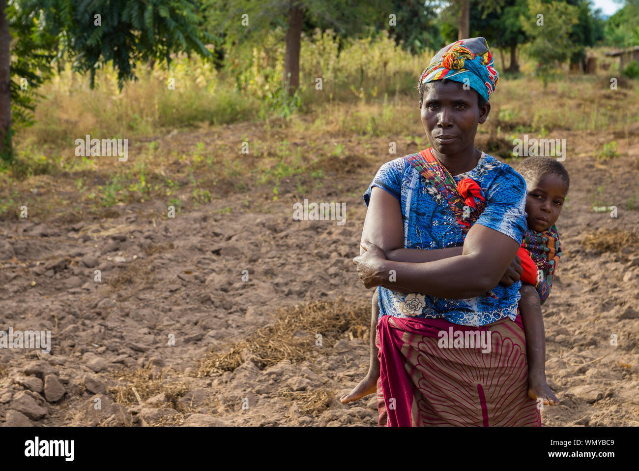 Une agricultrice avec son enfant sur son dos se trouve sur leur domaine agricole, la démonstration de l'agriculture de conservation au Malawi. Banque D'Images