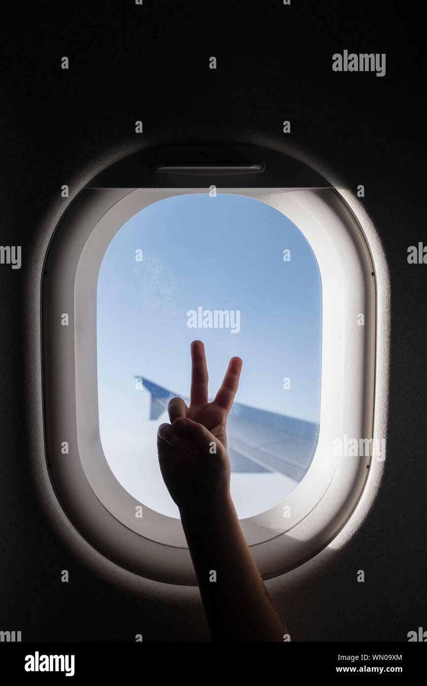 Silhouette de main de la jeune fille faisant signe de paix par la fenêtre de l'avion Banque D'Images Silhouette de main de la jeune fille faisant signe de paix par la fenêtre de l'avion Banque D'Images