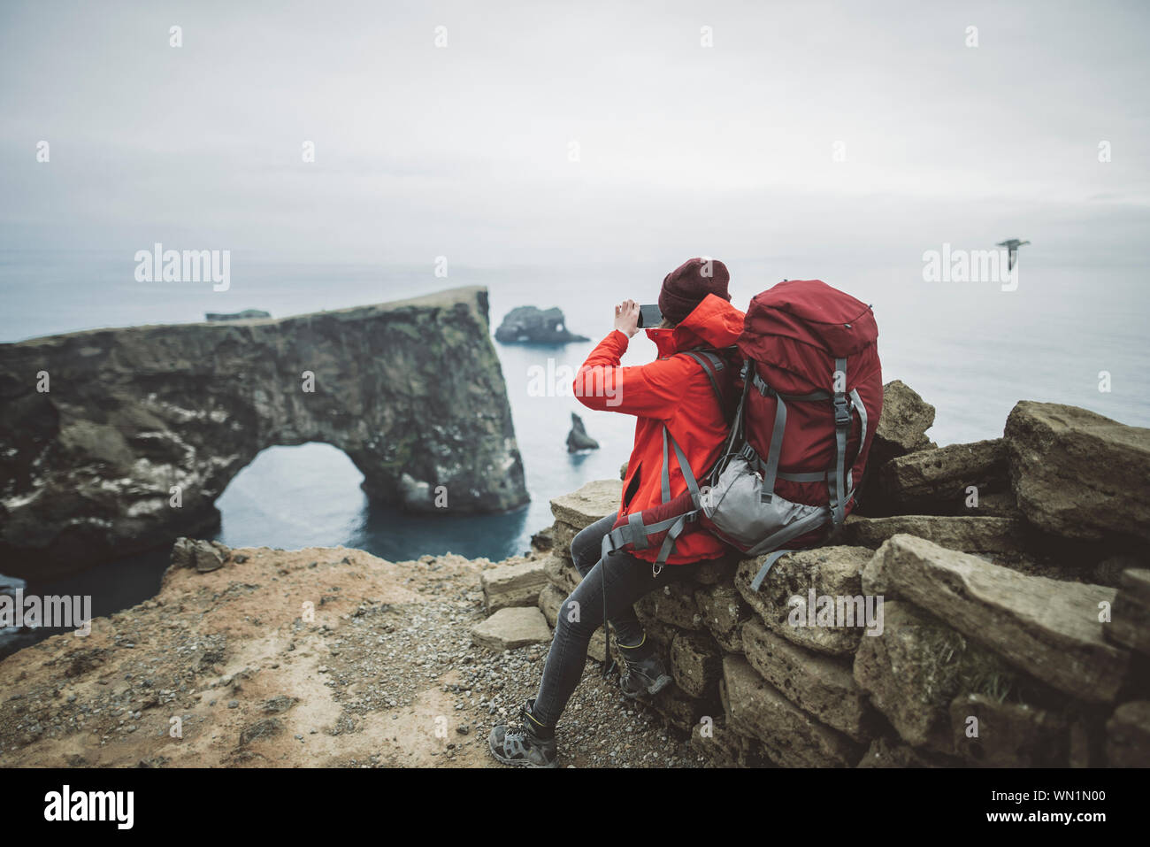 Female hiker photographing arche naturelle dans la région de Vik, Islande Banque D'Images