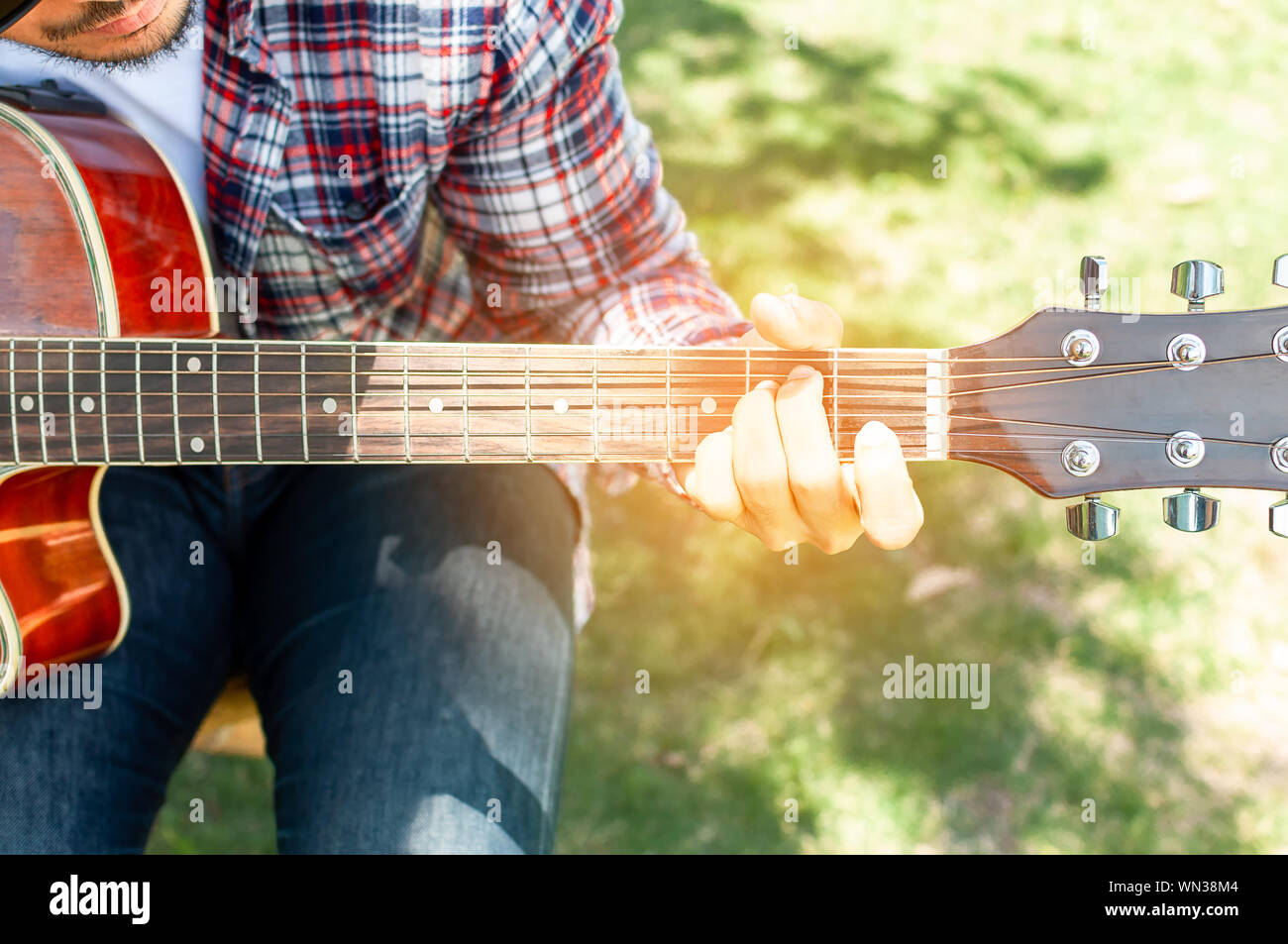 Le pays est l'homme qui joue de la guitare dans le jardin. Beau cowboy joue guitare folk song.Il porte des jeans et chemise scotch assis dans le domaine Banque D'Images