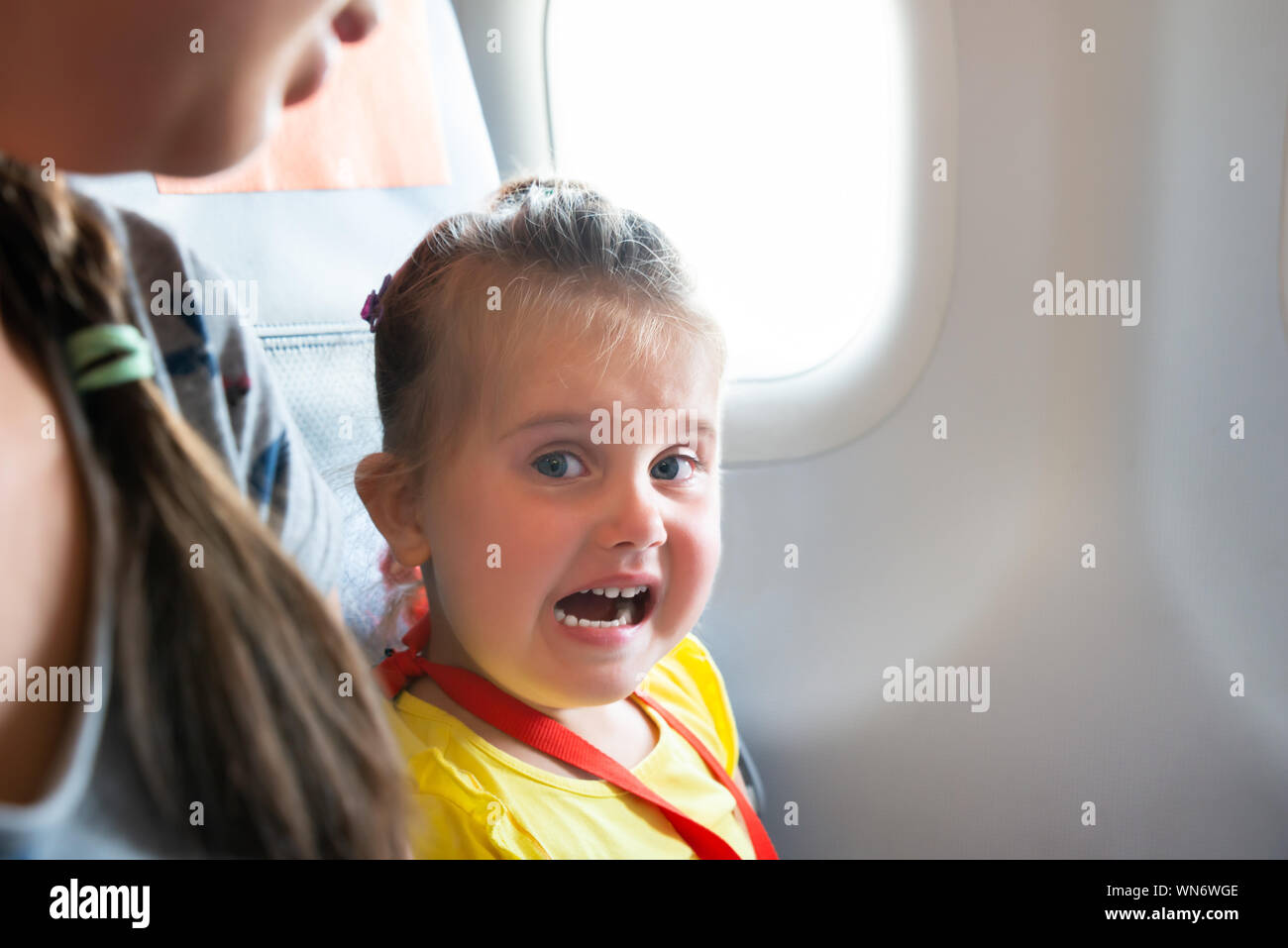 Petite fille assise à côté de Mère pleurer On Airplane Banque D'Images