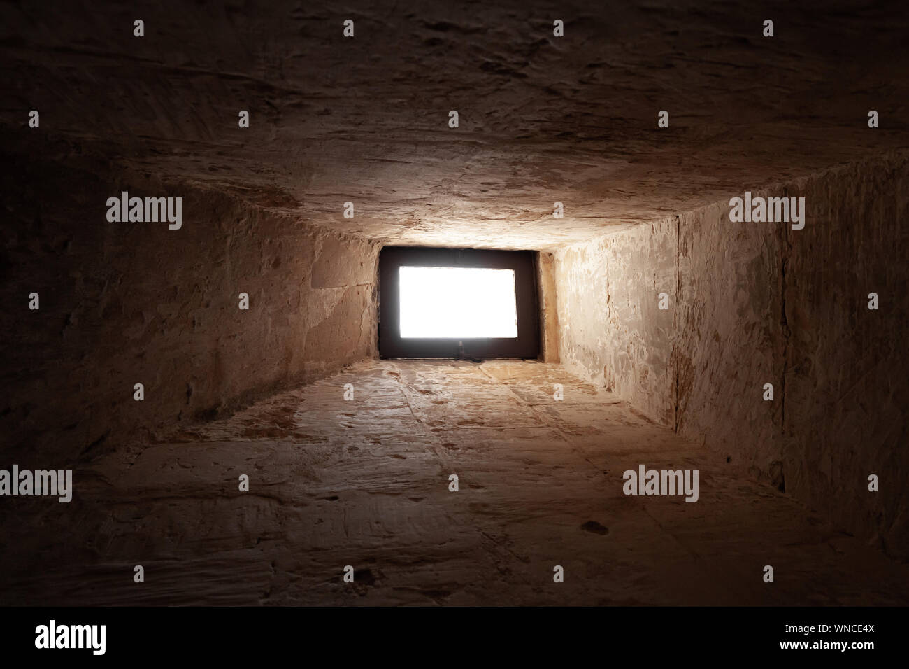 Petite fenêtre rayonnante en pierre sombre de l'intérieur. Résumé Contexte photo Banque D'Images