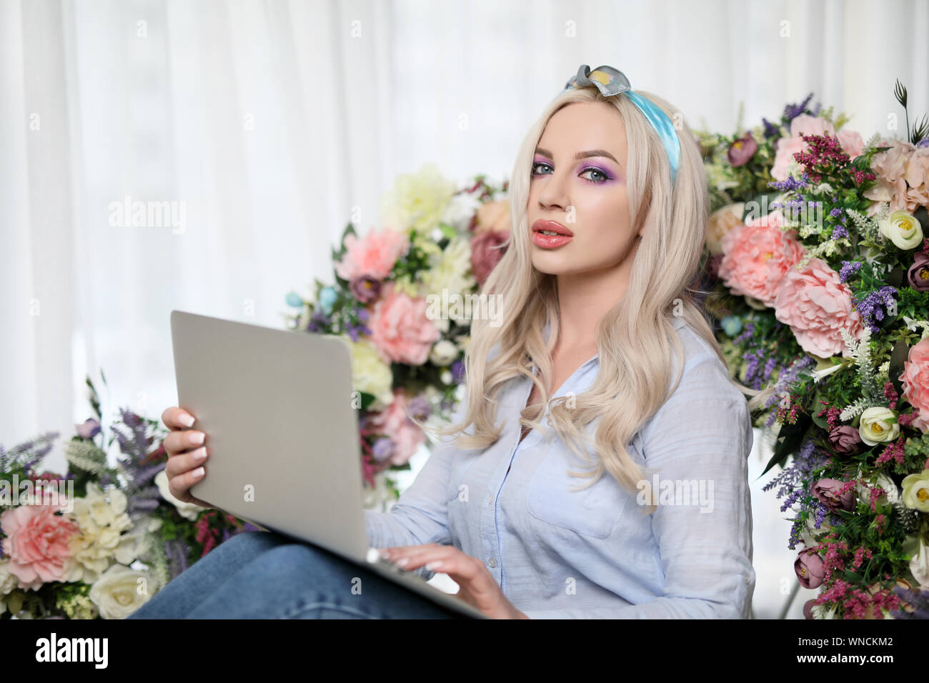 Belle fille blonde glamour , avec un ordinateur portable sur le lit orné de fleurs .close up Banque D'Images