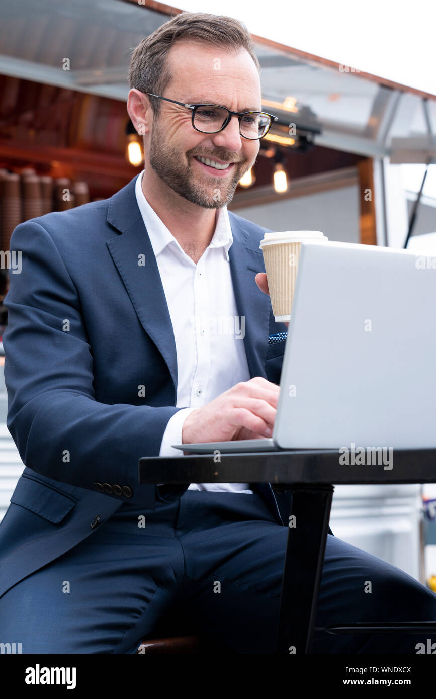 Mature Businessman Working On Laptop par Café-restaurant en plein air de boire du café à emporter Banque D'Images