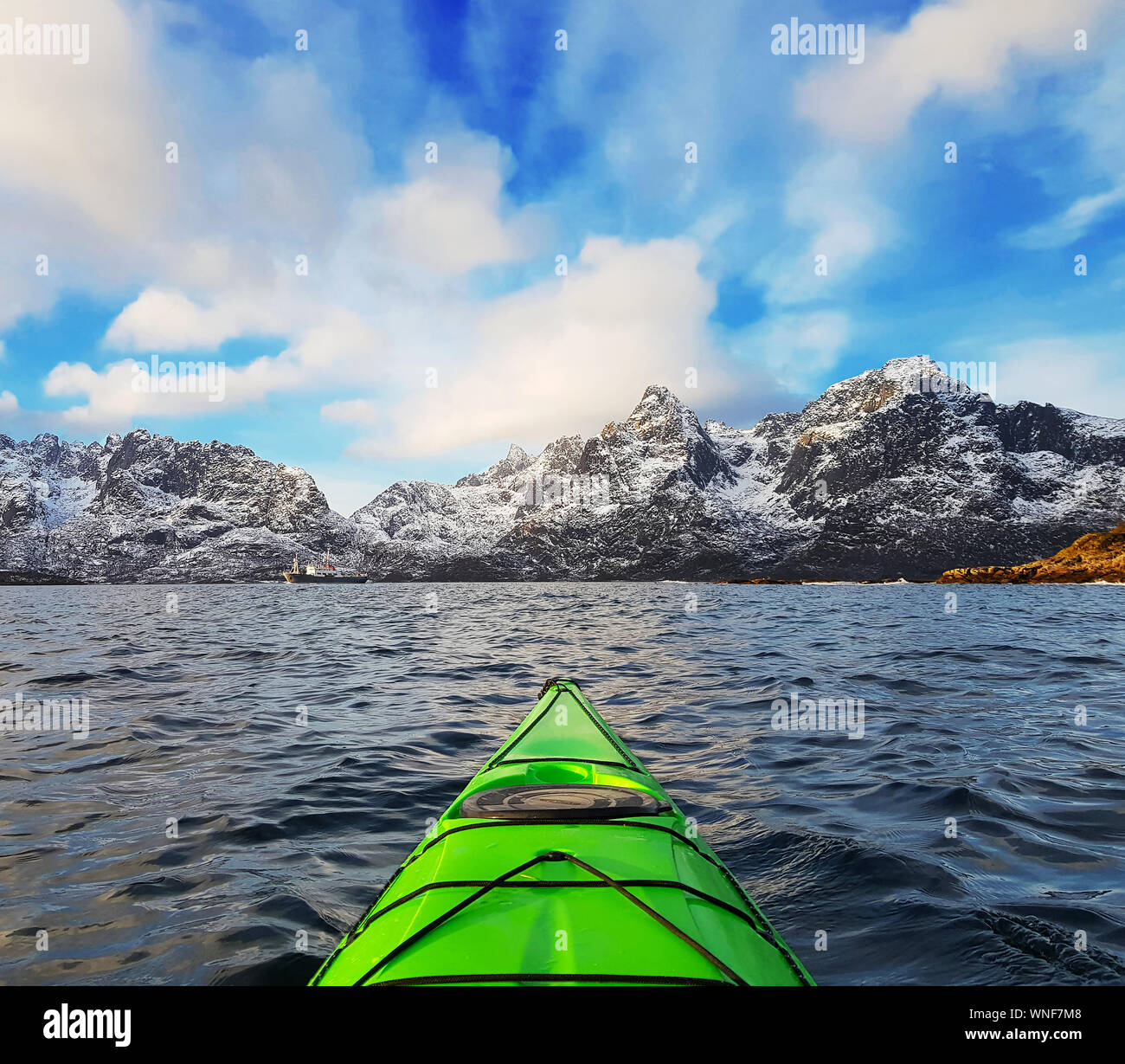Petit kayak dans le fjord de la baie verte dans les Lofoten, entouré de montagnes de neige et ciel bleu. La Norvège Banque D'Images
