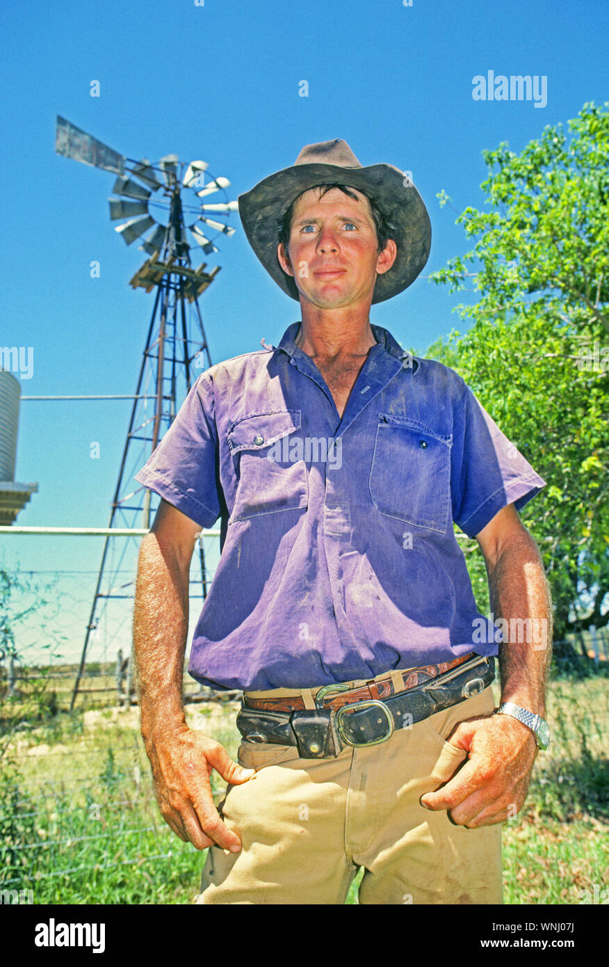 Le portrait d'un cow-boy australien en face d'un moulin à vent sur une grande station de bovins dans l'Outback du Queensland Banque D'Images