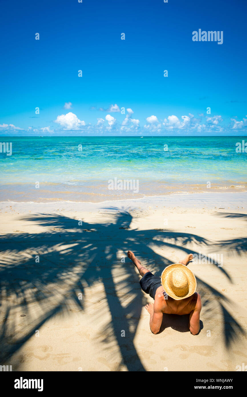 Tourisme décontracté portant un chapeau de paille couchée sur le rivage d'une île tropicale bordée de palmiers beach Banque D'Images