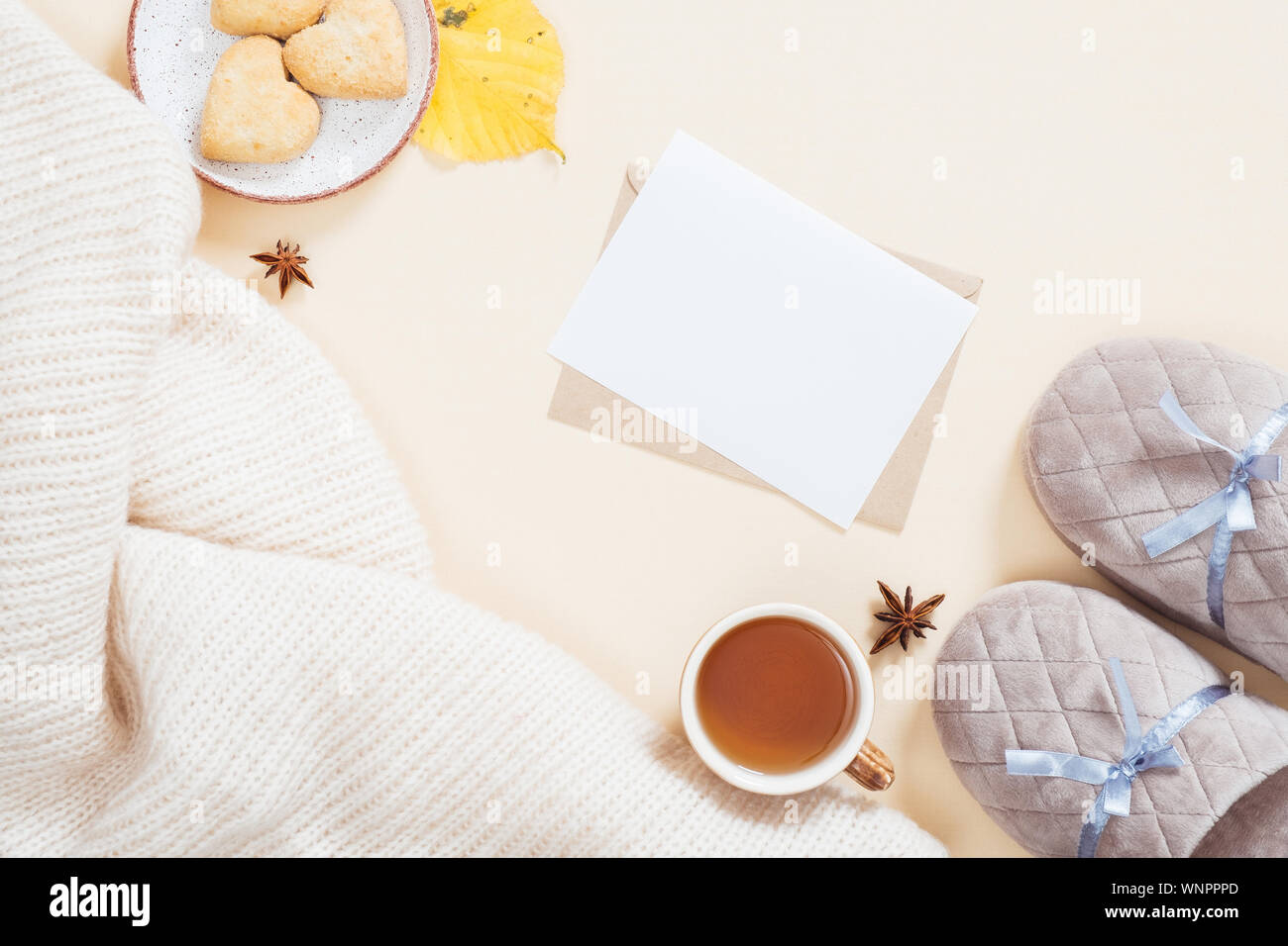Flatlay automne composition. Bureau féminin avec blanc à carreaux tricotés, une lettre, une boîte-cadeau, pantoufles, tasse de thé, de feuilles tombées sur fond beige pastel. Banque D'Images