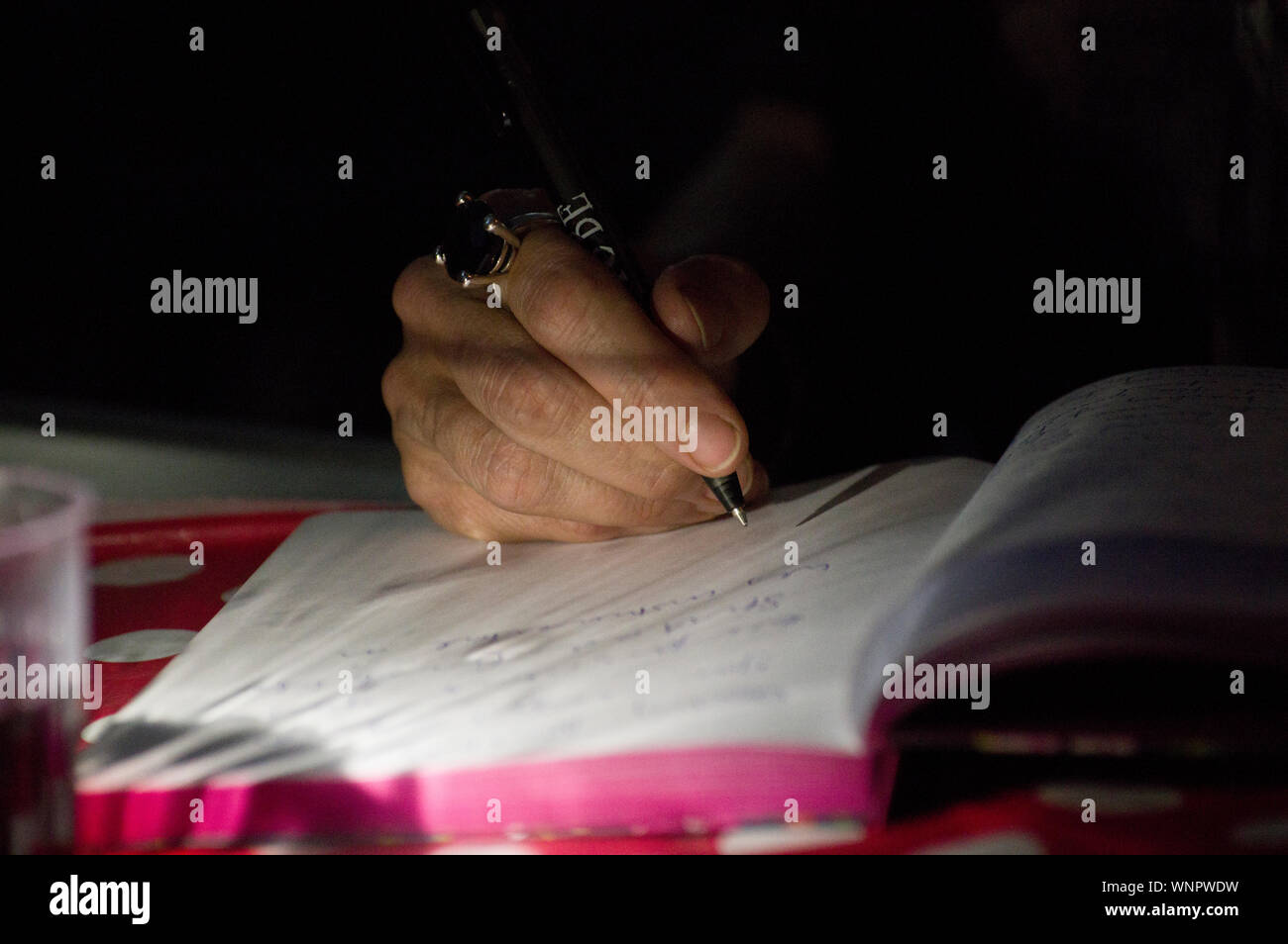 Plus la main de l'homme ou la femme avec un grand anneau de pierre gemme écrit dans un notebook Banque D'Images