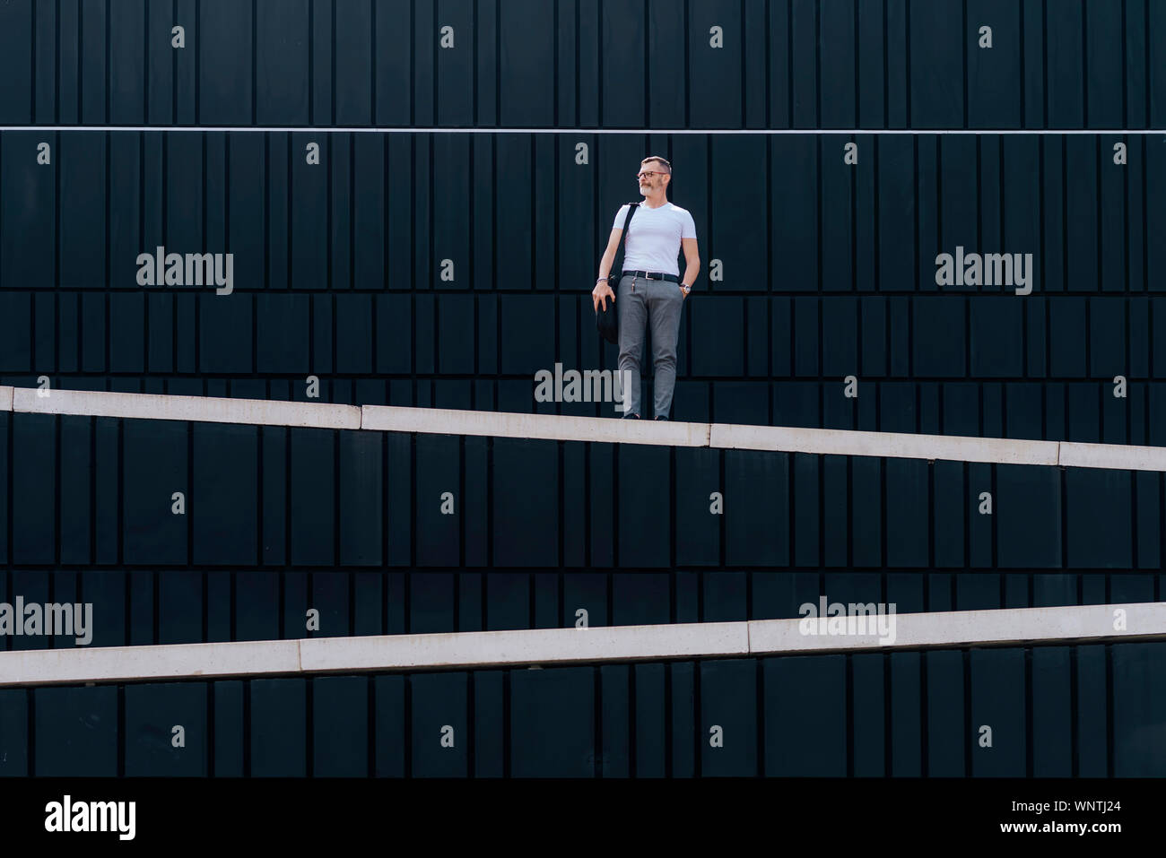 Homme barbu adultes avec bandoulière sac debout contre le mur de la ville Banque D'Images