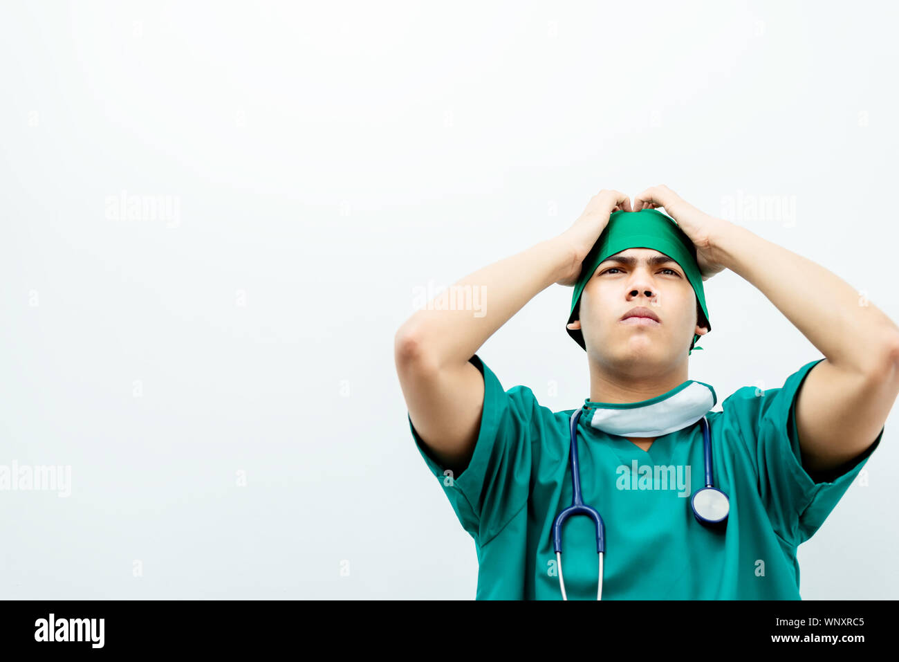 Jeune médecin asiatique sérieusement les mains des hommes sur le front du patient pour le traitement déçu .Médecin chirurgie en uniforme vert avec stéthoscope isolé sur Banque D'Images
