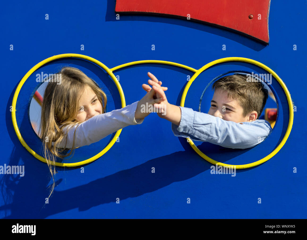 Garçon et fille de toucher avec la main. Les enfants mis tête par le trou à l'aire de jeux. Couple de jeunes enfants l'amour. Concept de l'amour et l'amitié. Banque D'Images