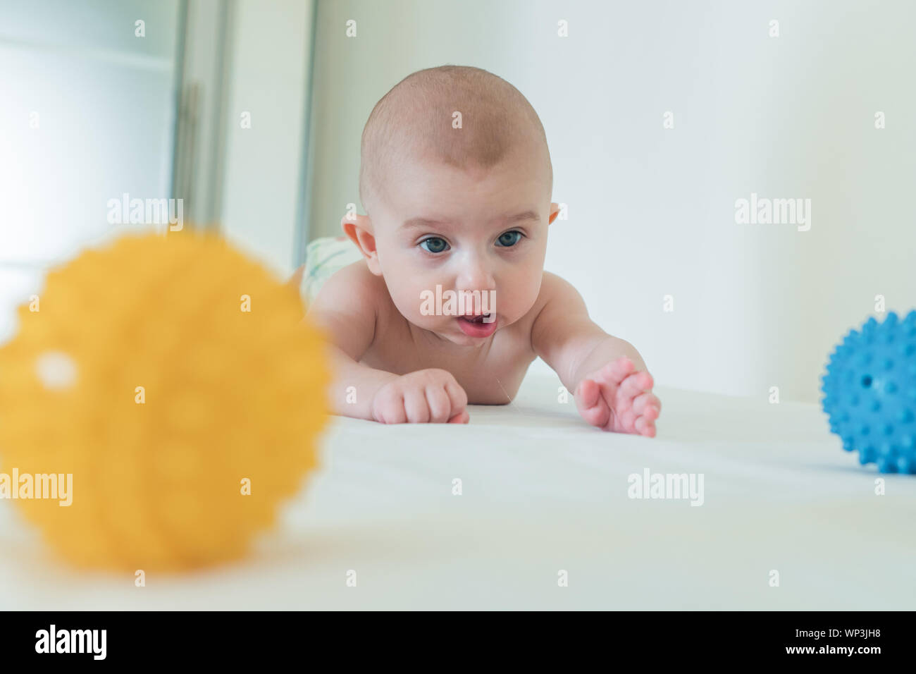 Un petit enfant se traîne sur la table à langer et de jouer une balle de caoutchouc. Banque D'Images