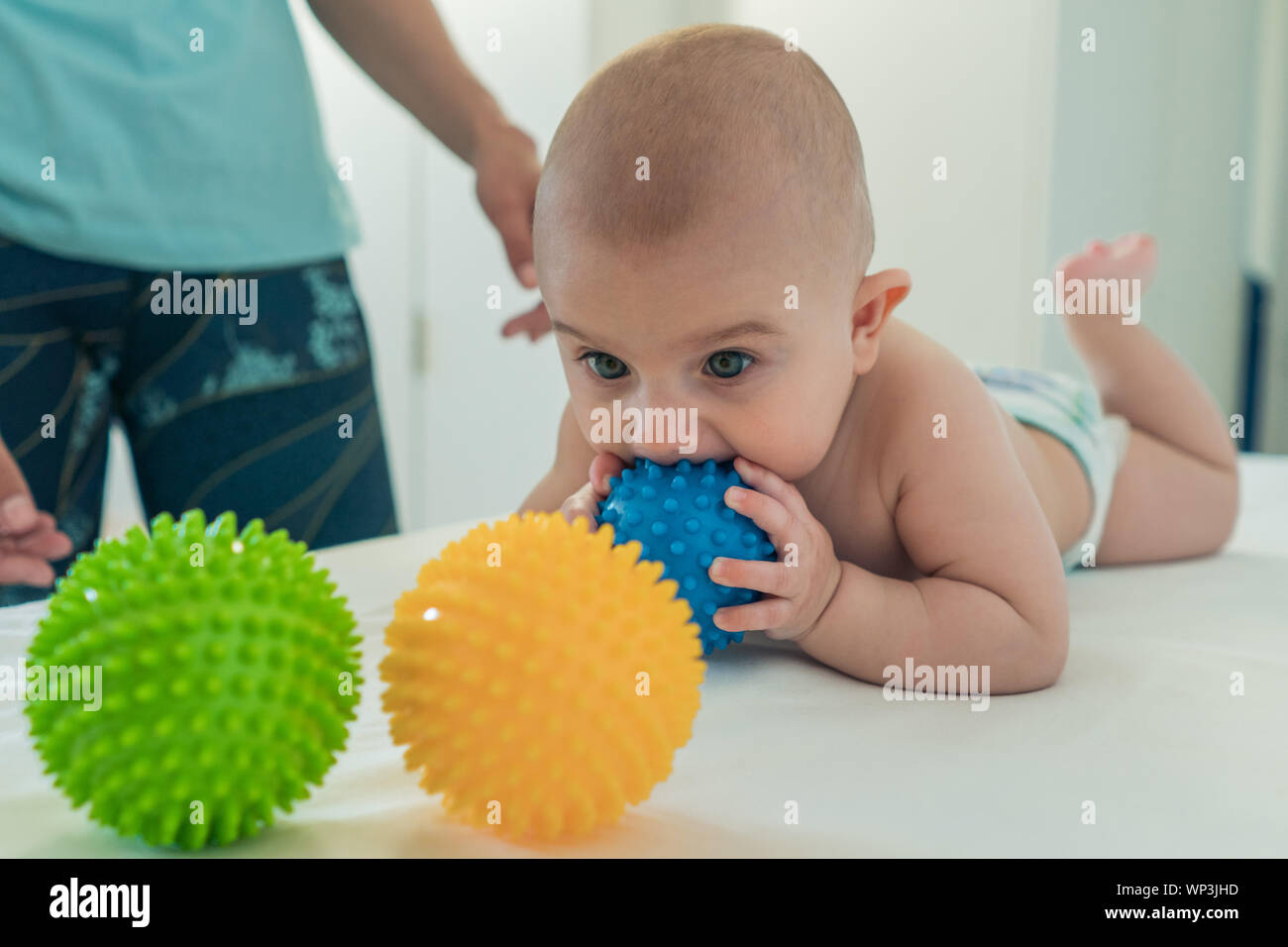 Un petit enfant se traîne sur la table à langer et les mâche une balle de caoutchouc. Banque D'Images