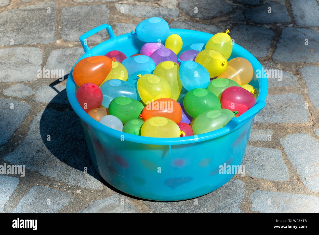 Cuve en plastique bleu rempli d'eau à base de bombes parti colorés ballons remplis avec de l'eau prêt pour un jeu pour enfants en plein air sur le pavage permanent Banque D'Images