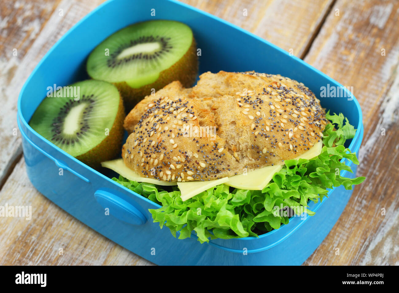 Rouleau complet avec du fromage et de la laitue avec deux moitiés de kiwi en bleu lunch box Banque D'Images