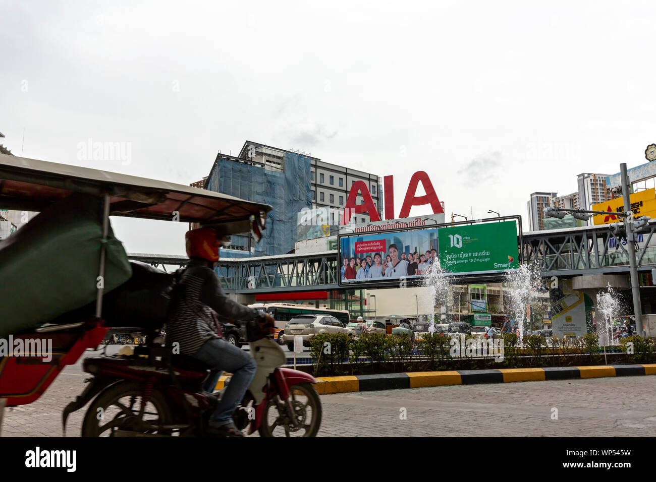 Le trafic est fluide sur une rue de ville en face d'un passage pour piétons menant à nouveau et moderne centre commercial Olympia à Phnom Penh, Cambodge. Banque D'Images