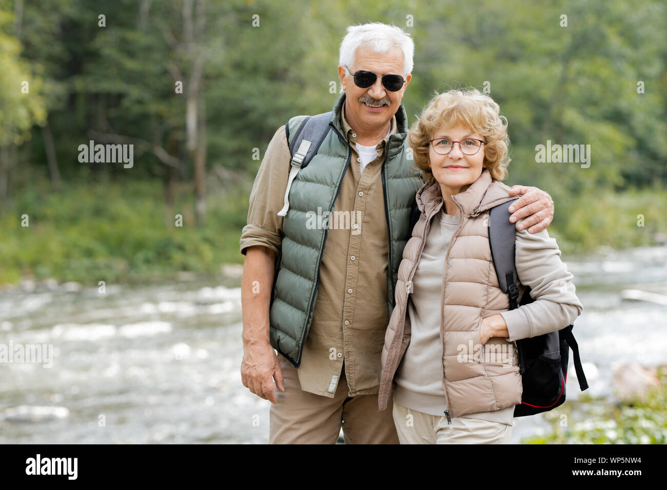 Mature couple actif avec des sacs en vous regardant par forest river Banque D'Images