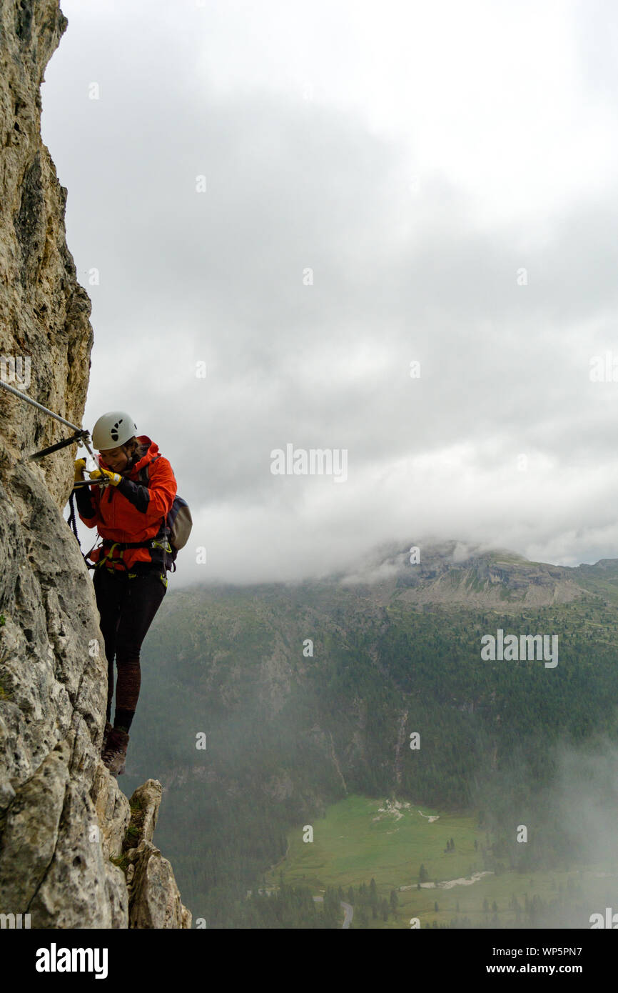 Belle jeune femme d'alpiniste sur une via ferrata dans les Dolomites de l'Italie dans le mauvais temps Banque D'Images