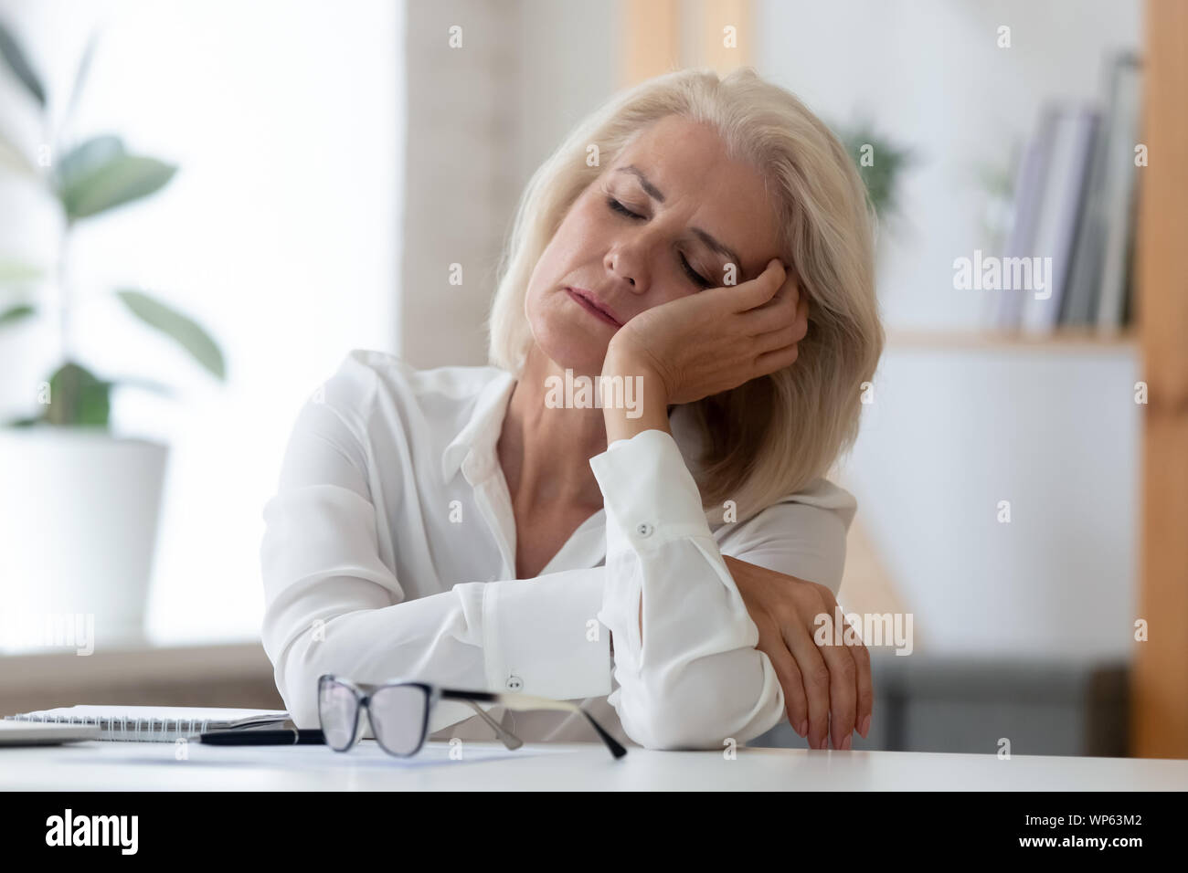 Épuisé senior businesswoman tomber endormi sur le lieu de travail Banque D'Images