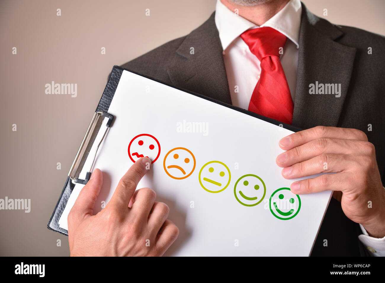 Homme en costume cravate avec un visage en colère montrant un émoticône dessinée sur une feuille. Composition horizontale. Vue avant Banque D'Images