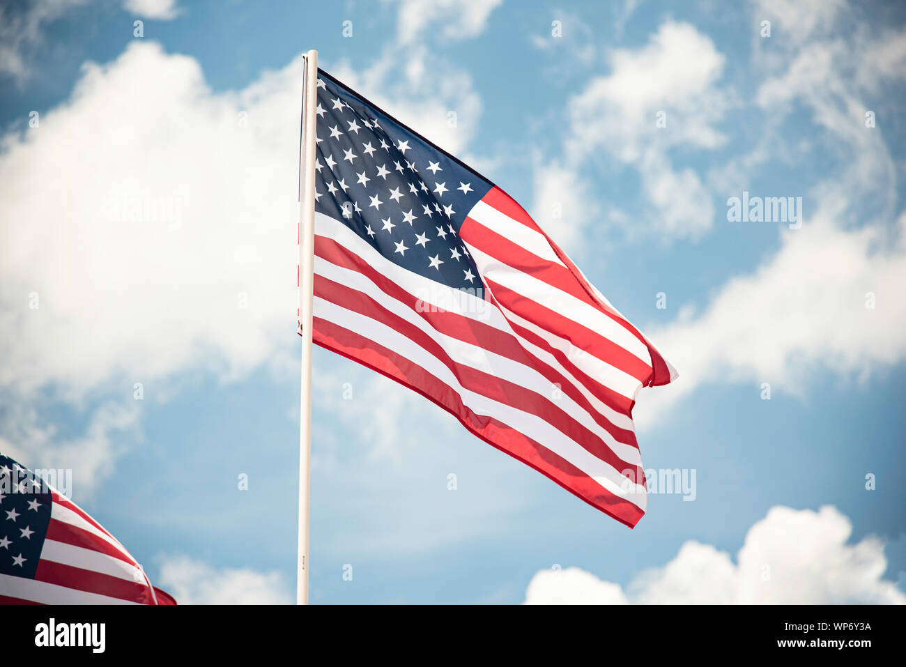 Deux drapeaux américains voletant dans le vent contre un ciel bleu avec des nuages blancs. Banque D'Images