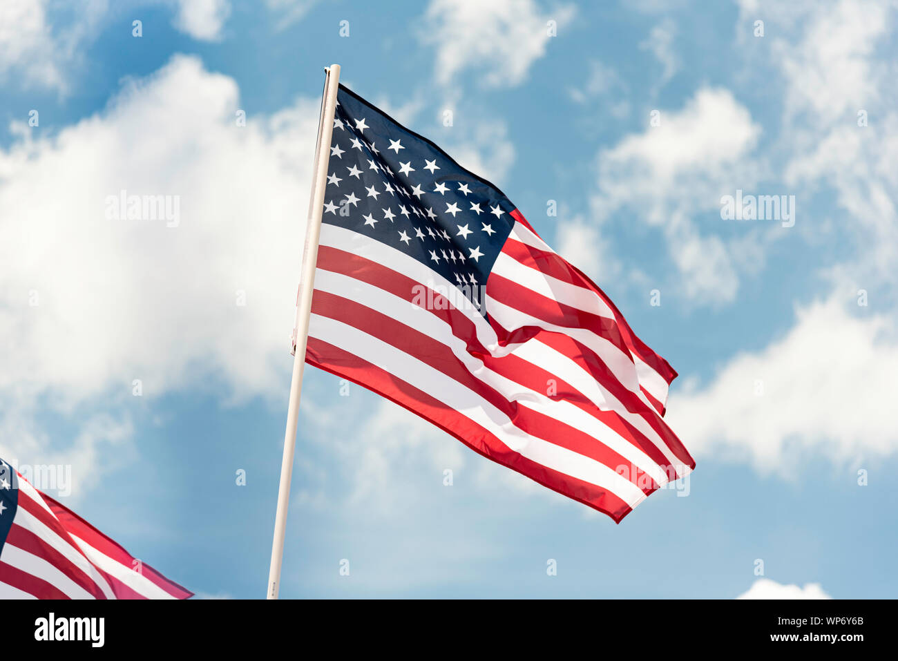 Deux drapeaux américains voletant dans le vent contre un ciel bleu avec des nuages blancs. Banque D'Images