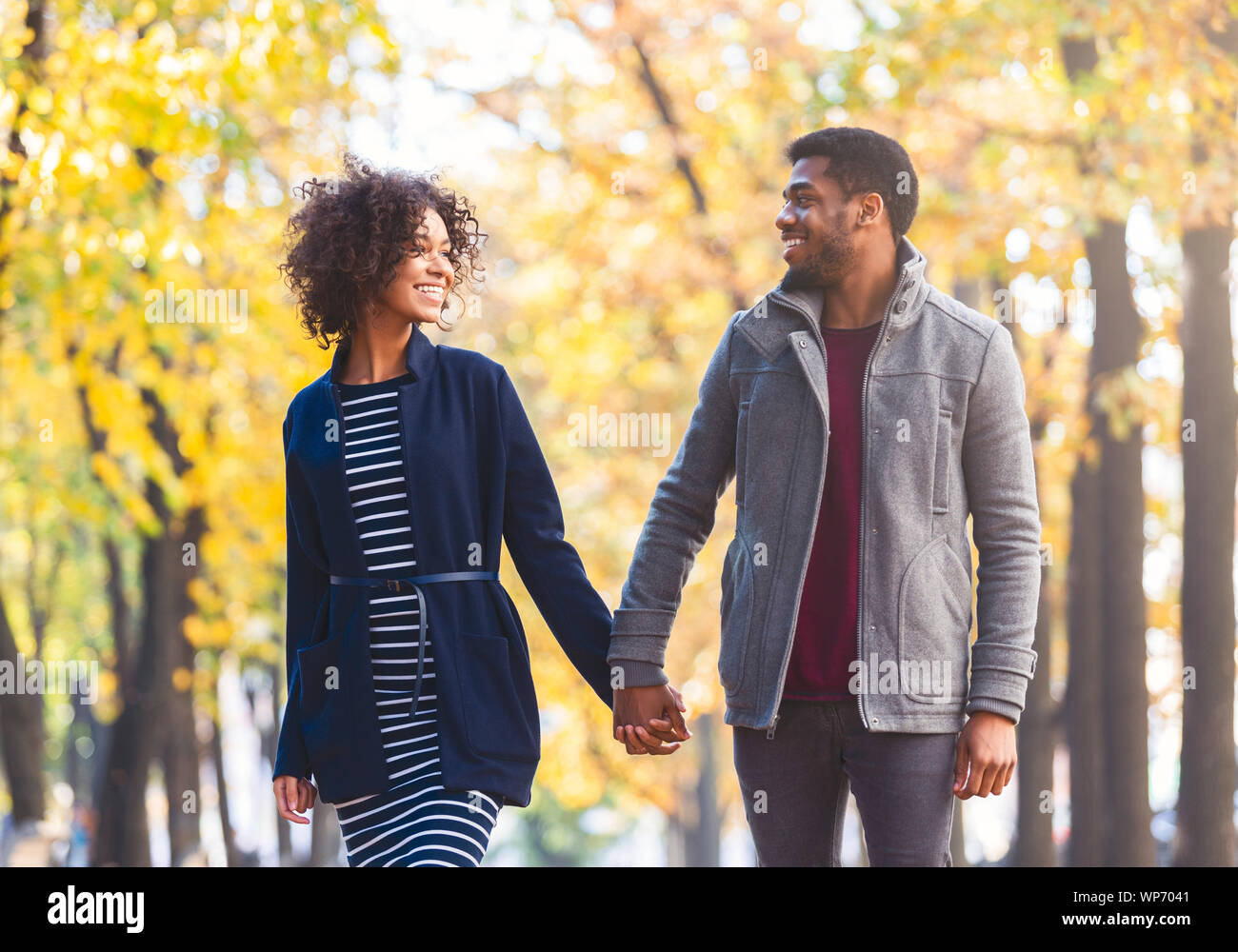 Black couple holding hands en marchant par autumn park Banque D'Images