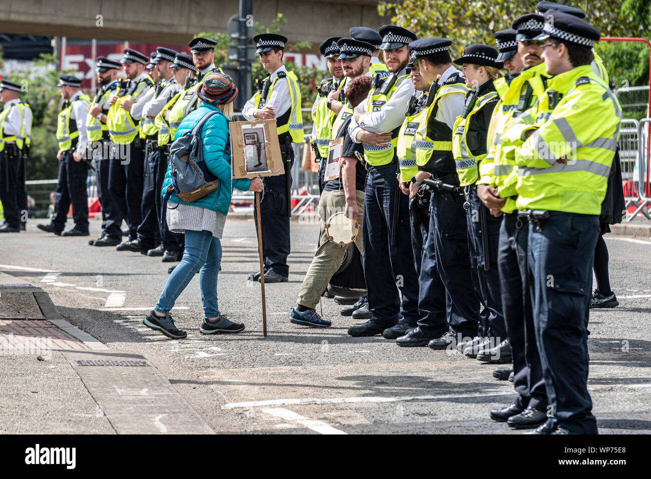 Petite femme manifestant avec cordon de police au sein de la Défense et Sécurité internationale de l'équipement Foire aux armements dees trade show, ExCel, Londres, UK Banque D'Images