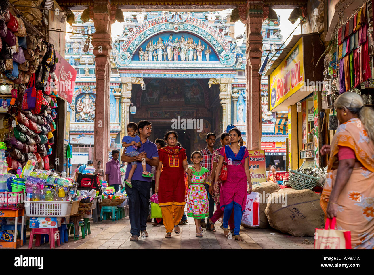 Madurai, Tamil Nadu / Inde - Janvier 14, 2016 : une famille indienne, promenades à travers une arche occupés par des boutiques, avec le célèbre Temple Meenakshi derrière. Banque D'Images
