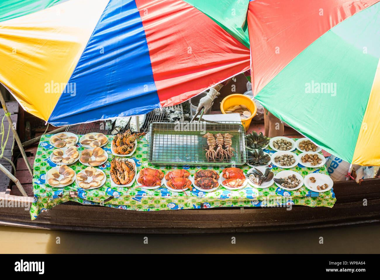 Samut Songkhram, Amphawa / Thaïlande - 15 juin 2019 : une table avec des fruits de mer grillés sous parasols colorés dans un bateau au marché flottant d'Amphawa. Banque D'Images