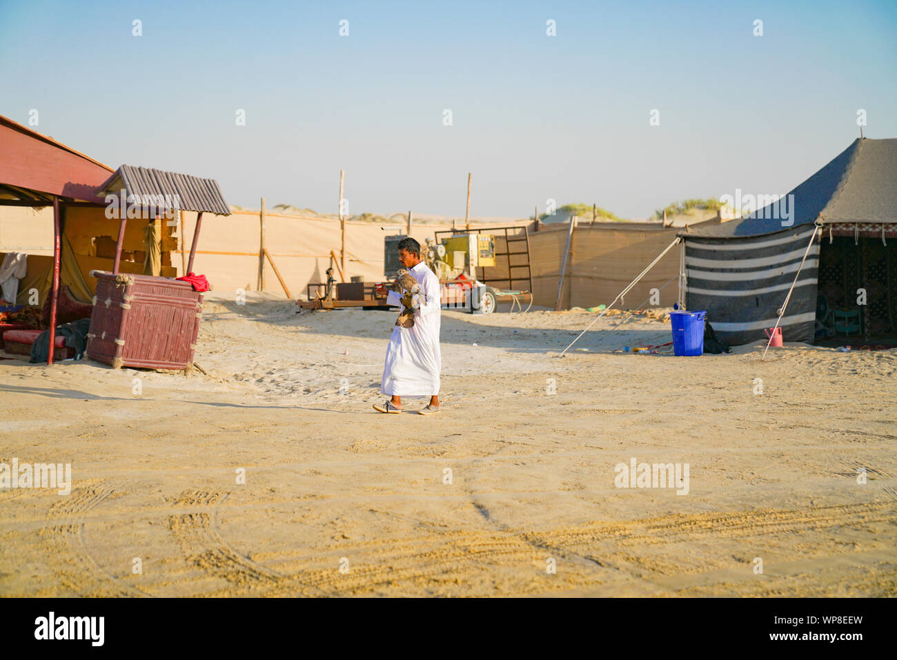 DOHA QATAR - le 12 juillet 2019 ; l'Arabe homme porte pèlerin sur bras de marcher entre les tentes dans la région de desert camp. Banque D'Images