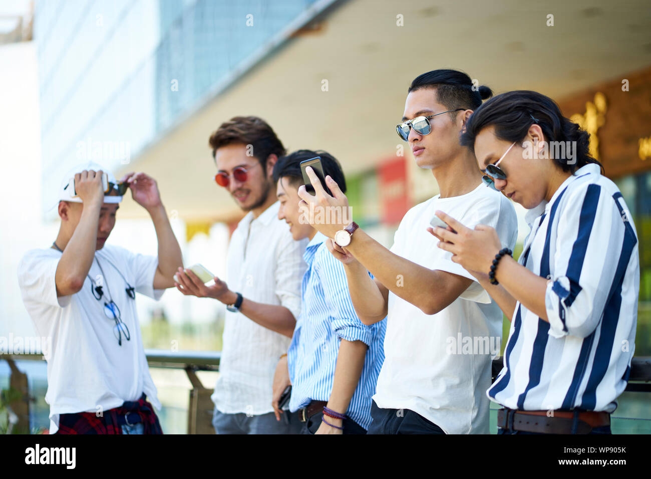 Groupe de cinq jeunes hommes asiatiques jouant avec les téléphones cellulaires à l'extérieur Banque D'Images
