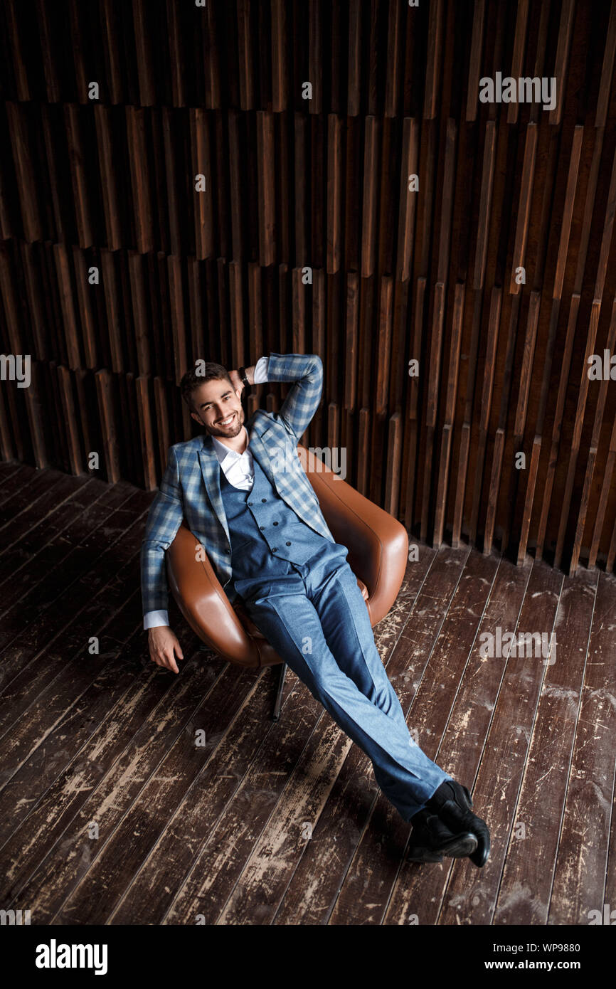 Jeune homme dans un costume bleu dans une cage est assis dans un fauteuil en cuir. jeune homme avec une barbe smiling Banque D'Images