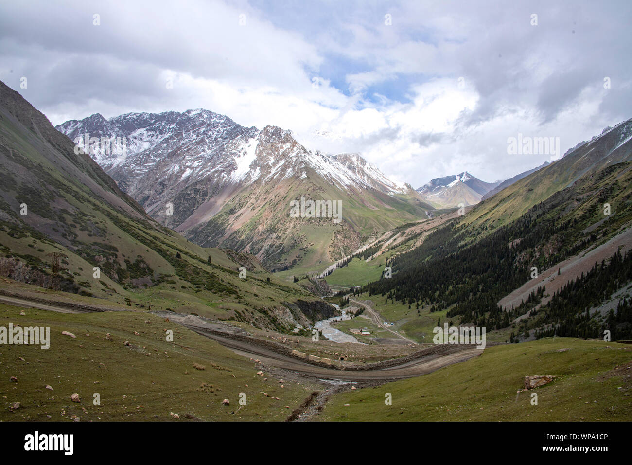 Route de montagne Serpentine près de la rivière dans la vallée, entre les collines couvertes de forêts de conifères et les pics couverts de neige. Banque D'Images