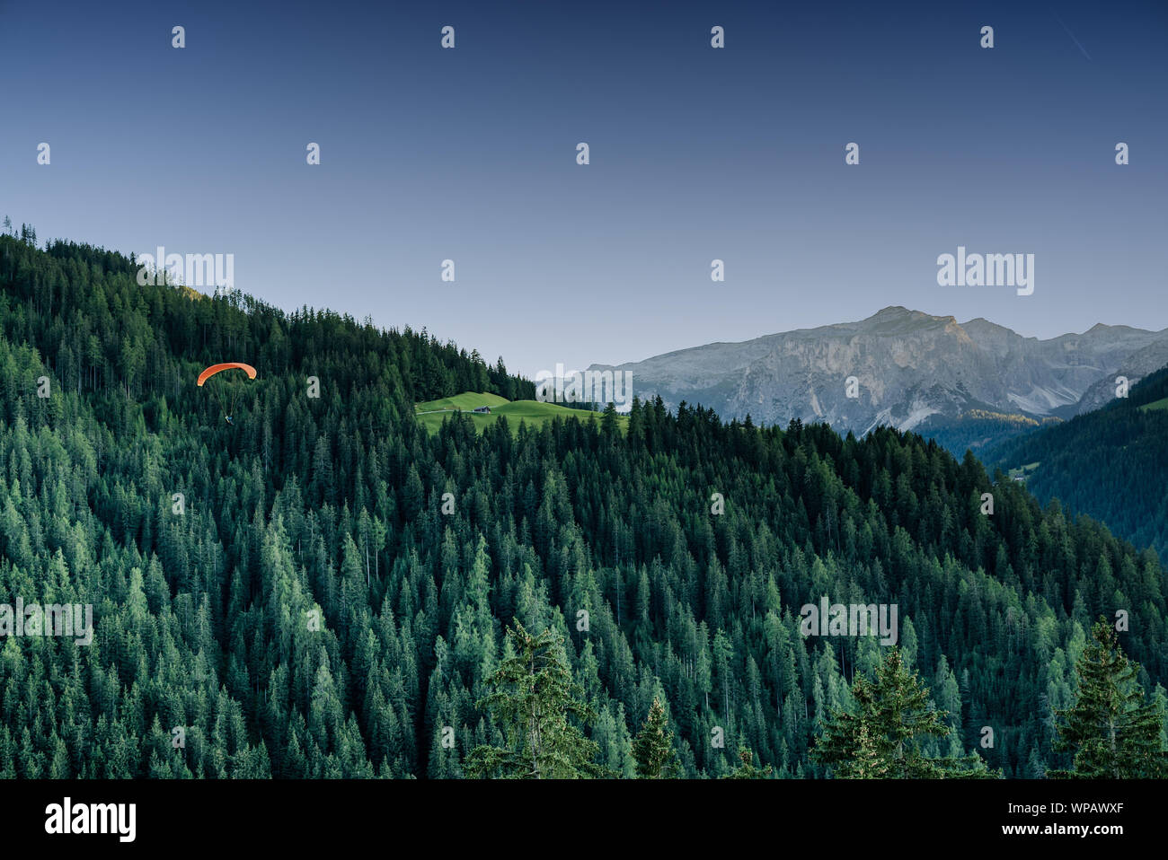 Parapente orange dans la dolomie de descendre dans un paysage de montagne de la vallée de la forêt au coucher du soleil Banque D'Images