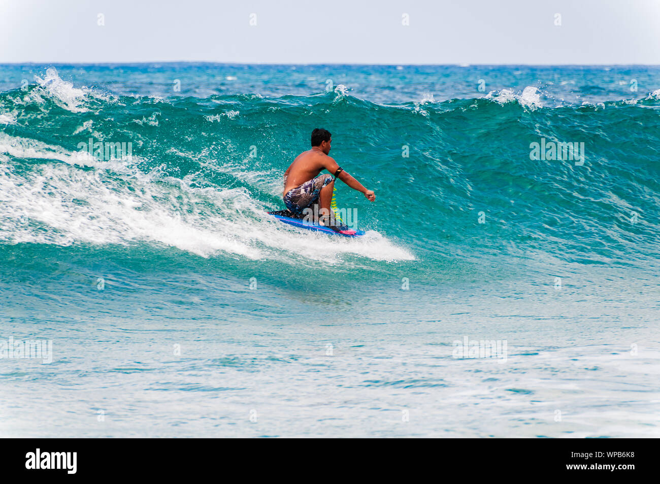 KOLOA, Kauai, HI - 24 AVRIL 2008 - Jeune homme monté sur une planche de surf dans une vague bleue à l'été. Banque D'Images