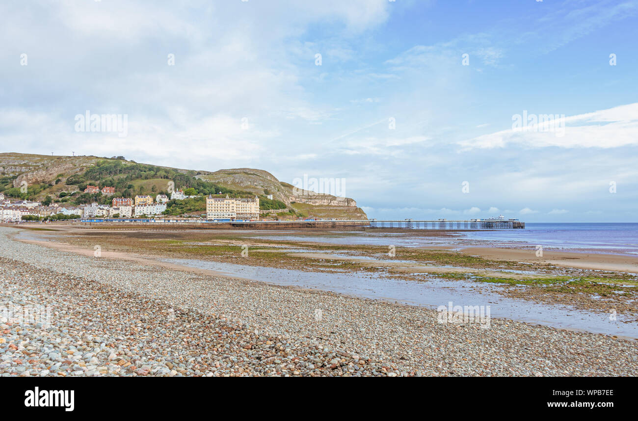 Une vue de la rive et courbée du Llandudno pier. Le grand orme pointe est dans la distance et un ciel bleu est au-dessus. Banque D'Images