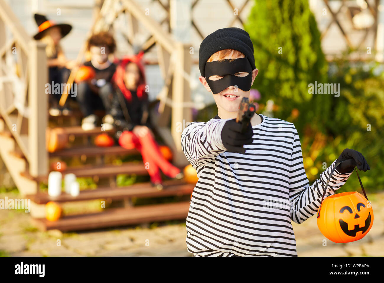 Waist up portrait of cute boy habillé en posant à l'extérieur sur bandit holding Halloween Pumpkin panier et pointing gun at camera, copy space Banque D'Images