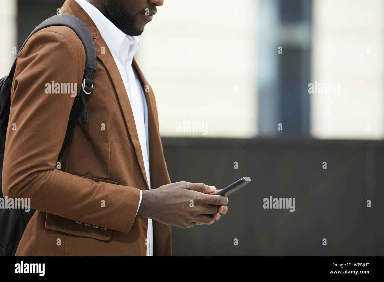 Mid section Vue de côté de l'homme afro-américain holding smartphone et la saisie des messages texte en milieu urbain, copy space Banque D'Images