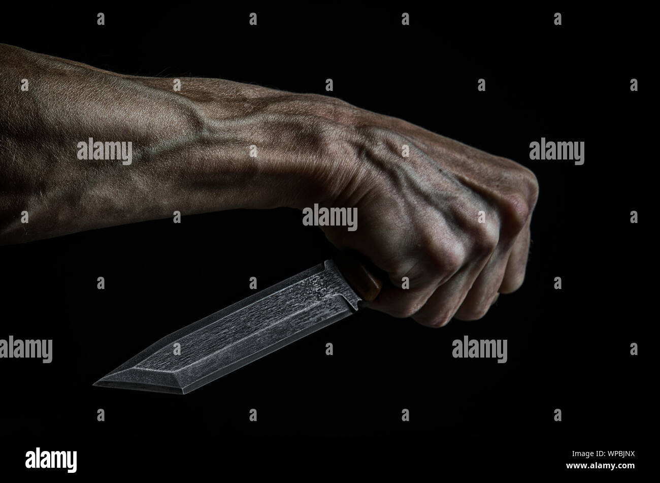 Un homme avec un couteau à la main dans l'obscurité. Banque D'Images