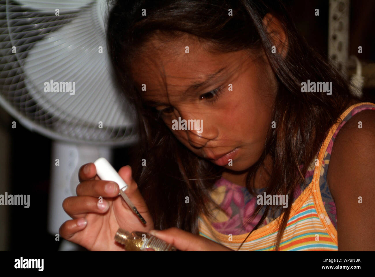 Jeune fille aux cheveux brun noir peinture ses ongles ongles avec une piscine avec un airfan polonais dans l'arrière Banque D'Images