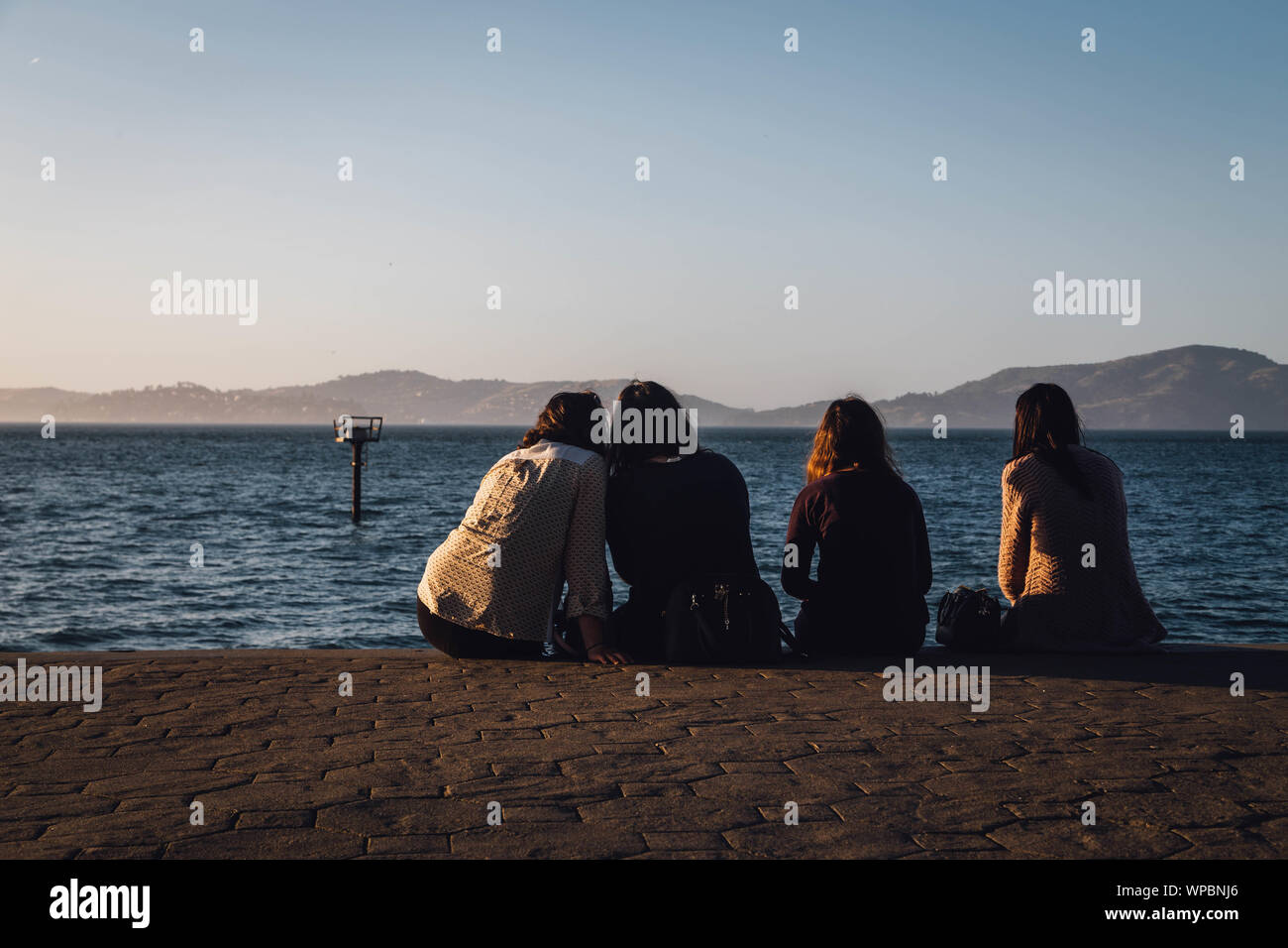 Quatre amies, profiter d'un coucher de soleil de San Francisco s'assit au bord de la bay Banque D'Images