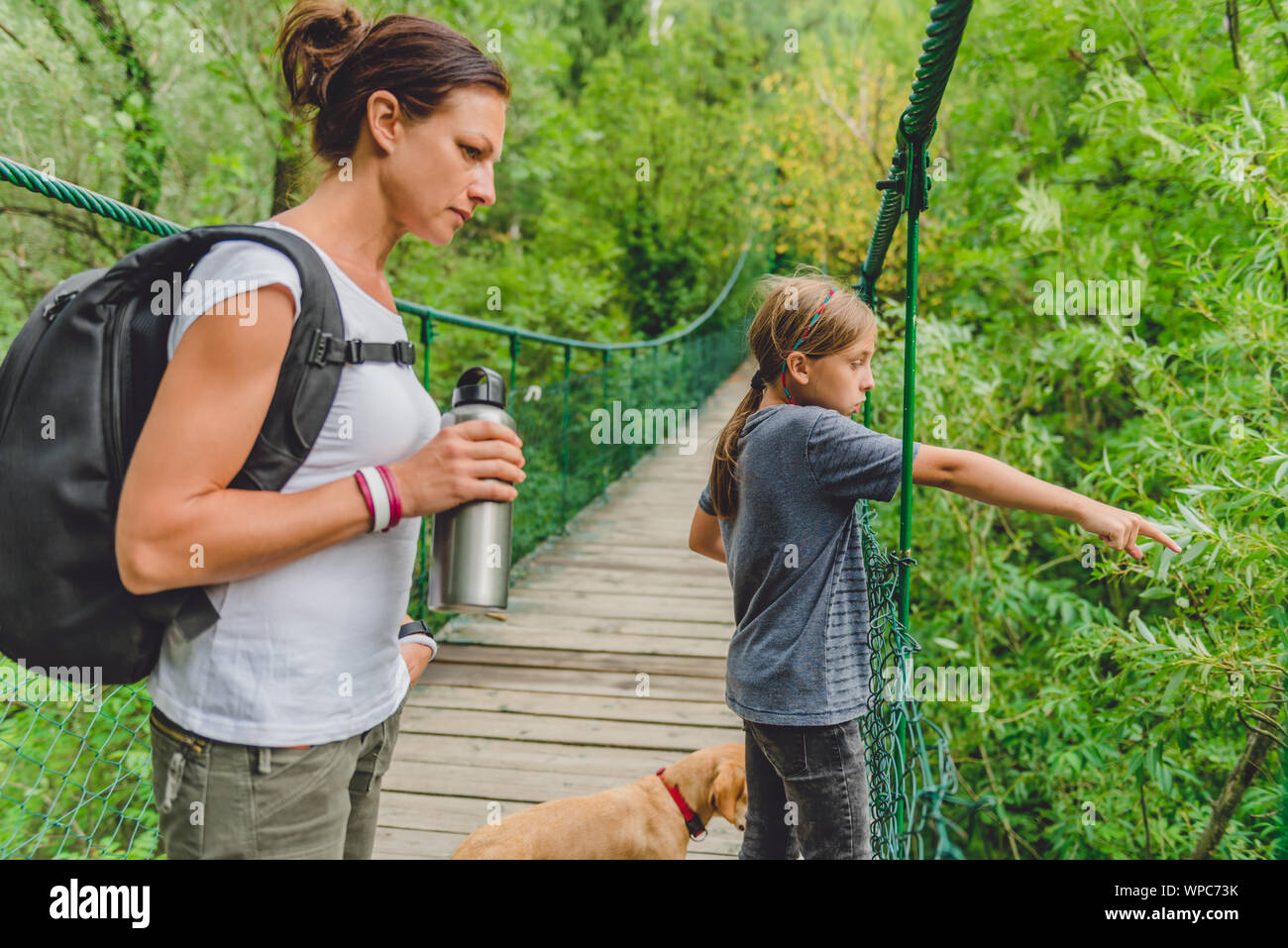 Mère et fille debout sur le pont suspendu en bois avec petit chien jaune et à la recherche à la rivière ci-dessous Banque D'Images Mère et fille debout sur le pont suspendu en bois avec petit chien jaune et à la recherche à la rivière ci-dessous Banque D'Images