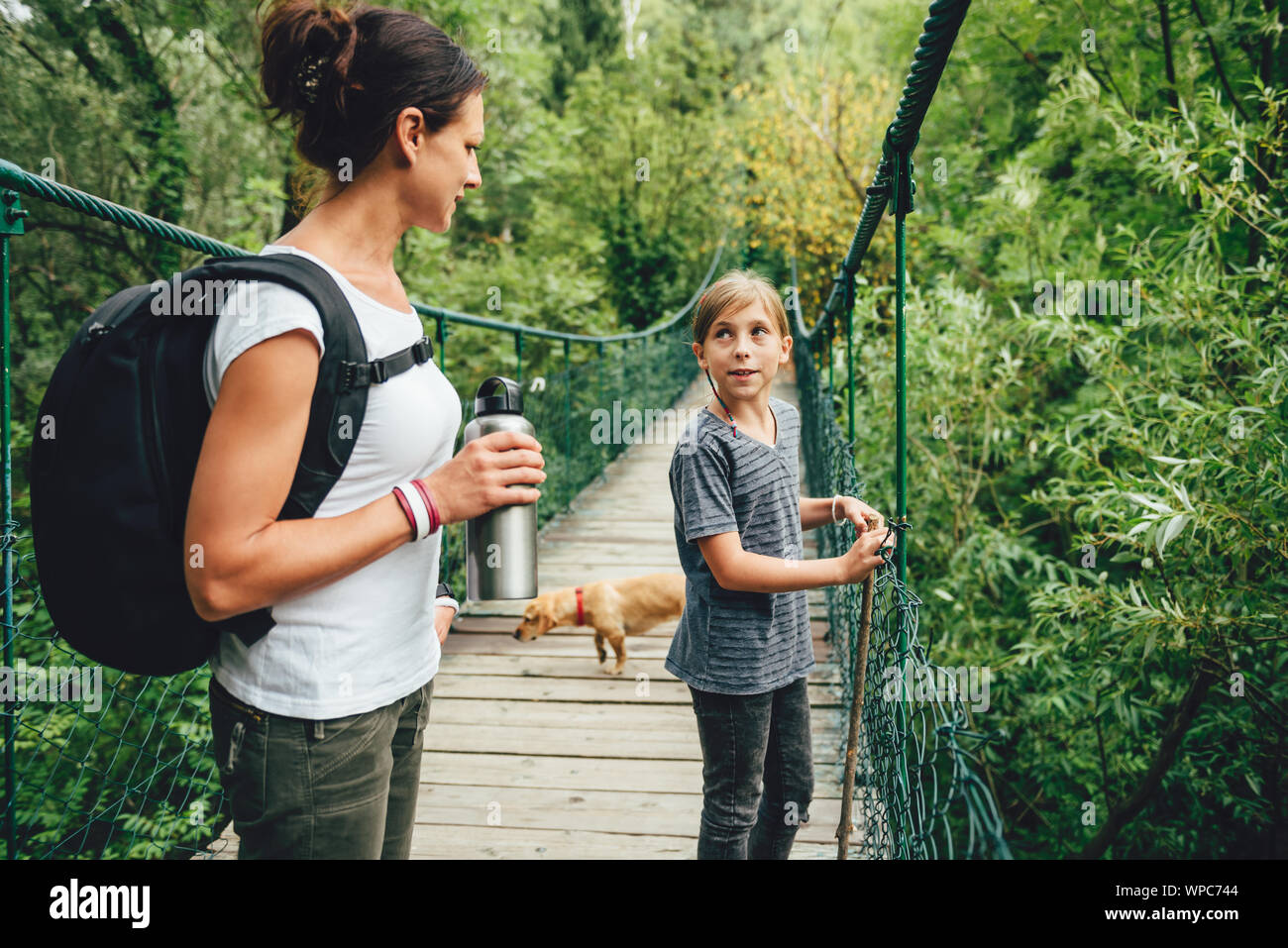 Mère et fille debout sur le pont suspendu en bois avec petit chien jaune et de parler Banque D'Images Mère et fille debout sur le pont suspendu en bois avec petit chien jaune et de parler Banque D'Images